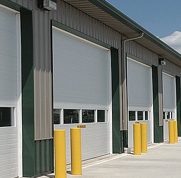 Row of white commercial overhead doors with protective bollards