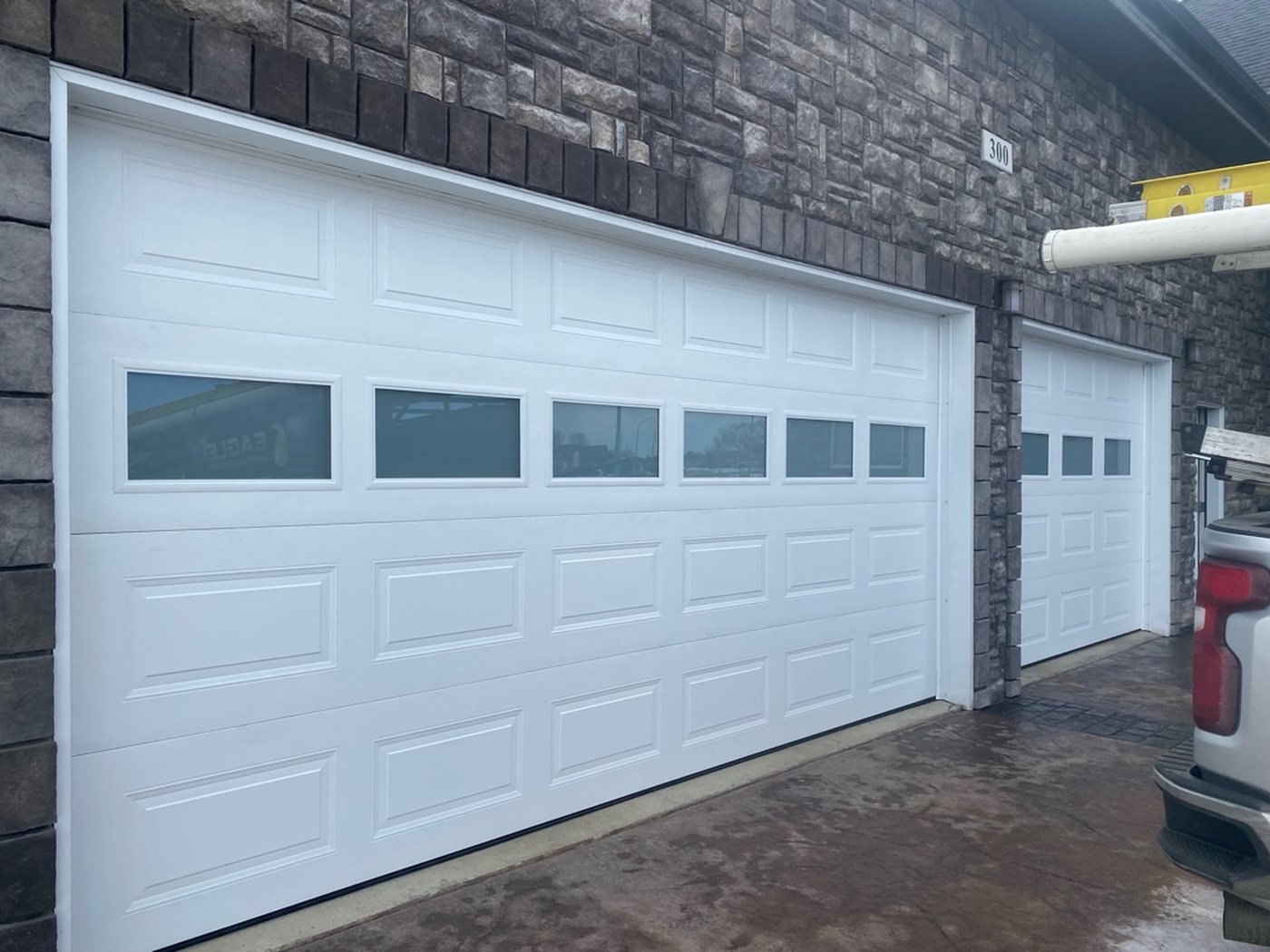 Wide white sectional door with a window row inside a stone-clad shop